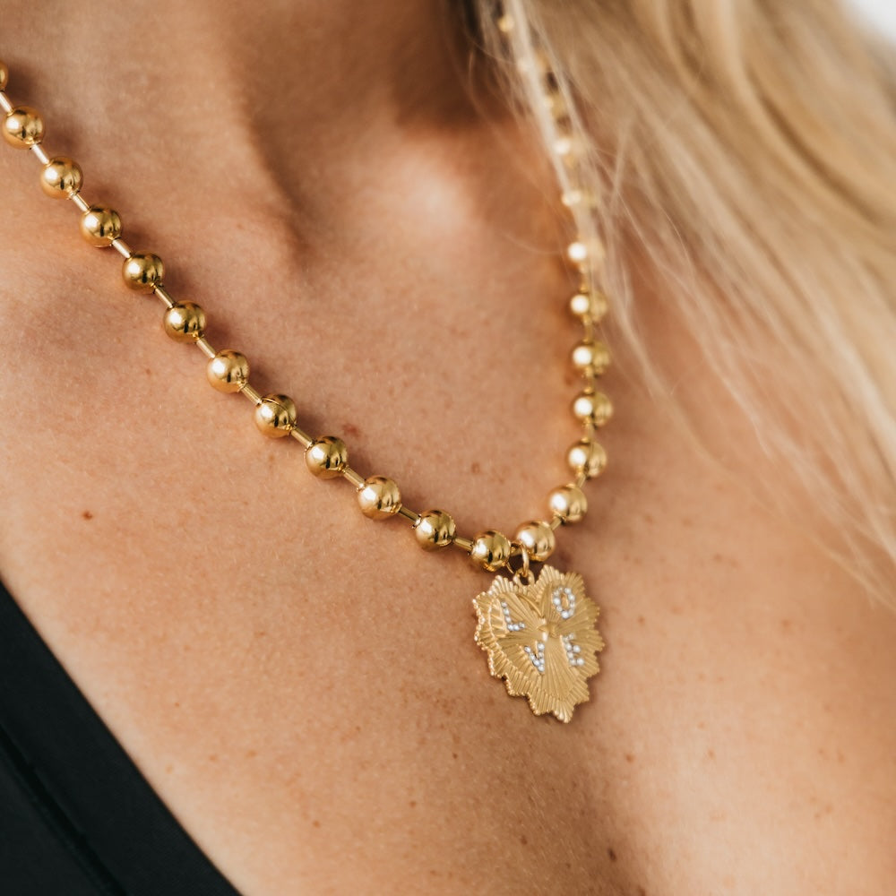 Gold-tone beaded ball chain necklace with sunburst heart pendant at center