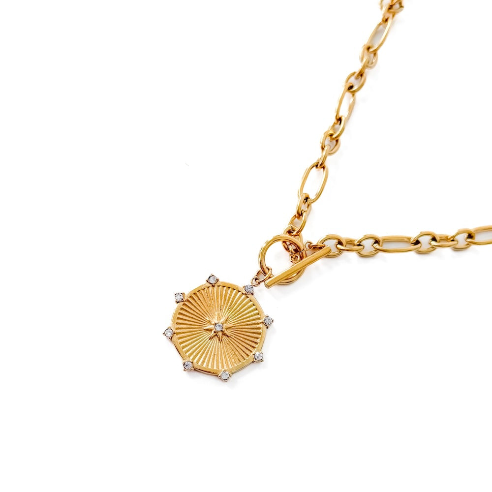 Close-up gold-tone chain with round sunburst pendant and clear stones