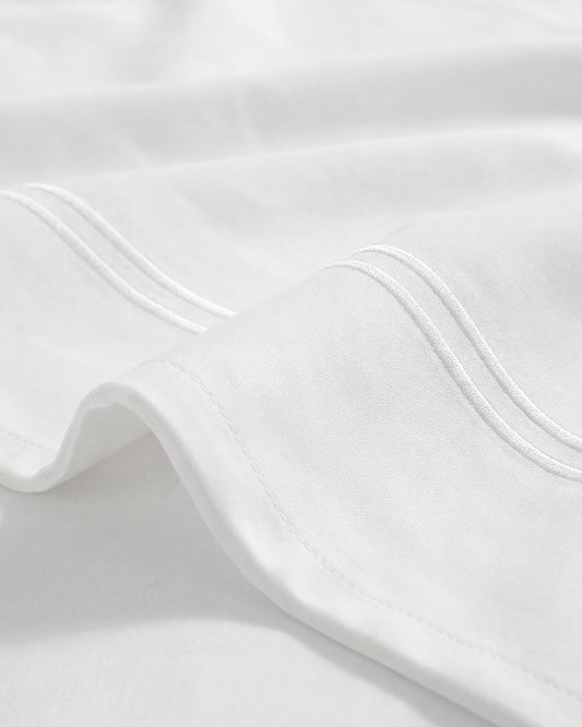 White top sheet corner with neat embroidered edge and double-stitching detail.