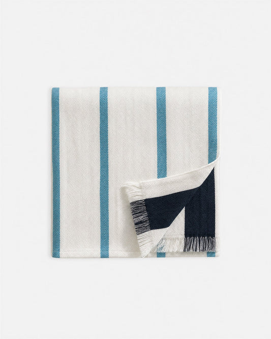 Off-white beach blanket with vertical blue and navy stripes, fringed hem