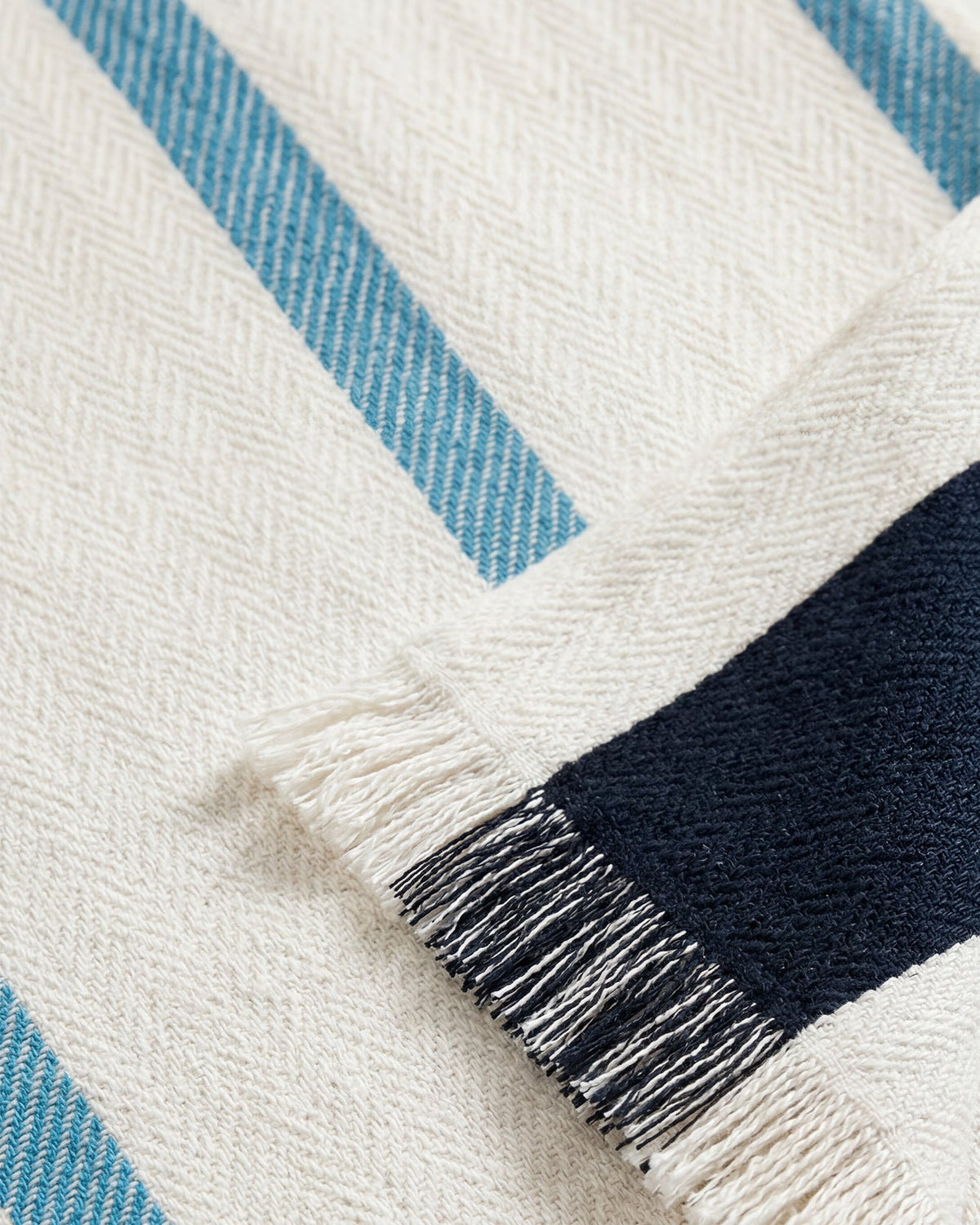 Corner close-up of striped beach blanket with navy-blue and off-white fringe