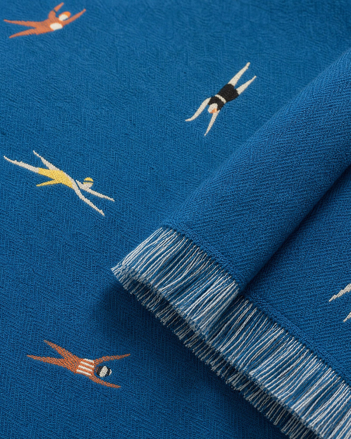 Close-up of aqua-blue beach blanket fabric with colorful swimmers and fringed border