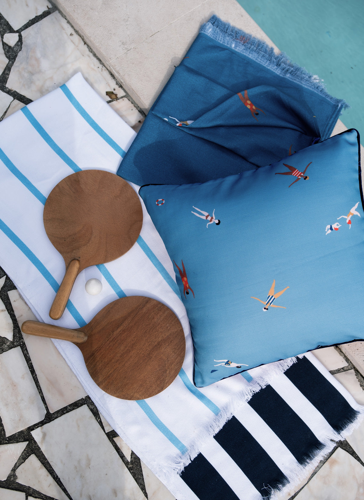 Folded aqua-blue beach blanket with colorful swimmer print, shown with striped towels