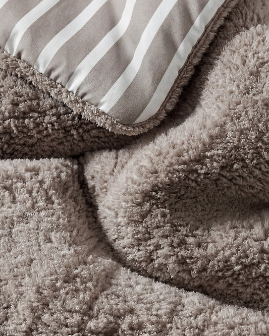 Close-up of taupe shaggy comforter texture with striped top panel and piping edge.