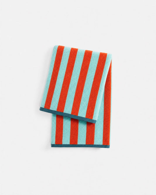 Reversible beach towel with aqua and orange vertical stripes, folded with a dark edge