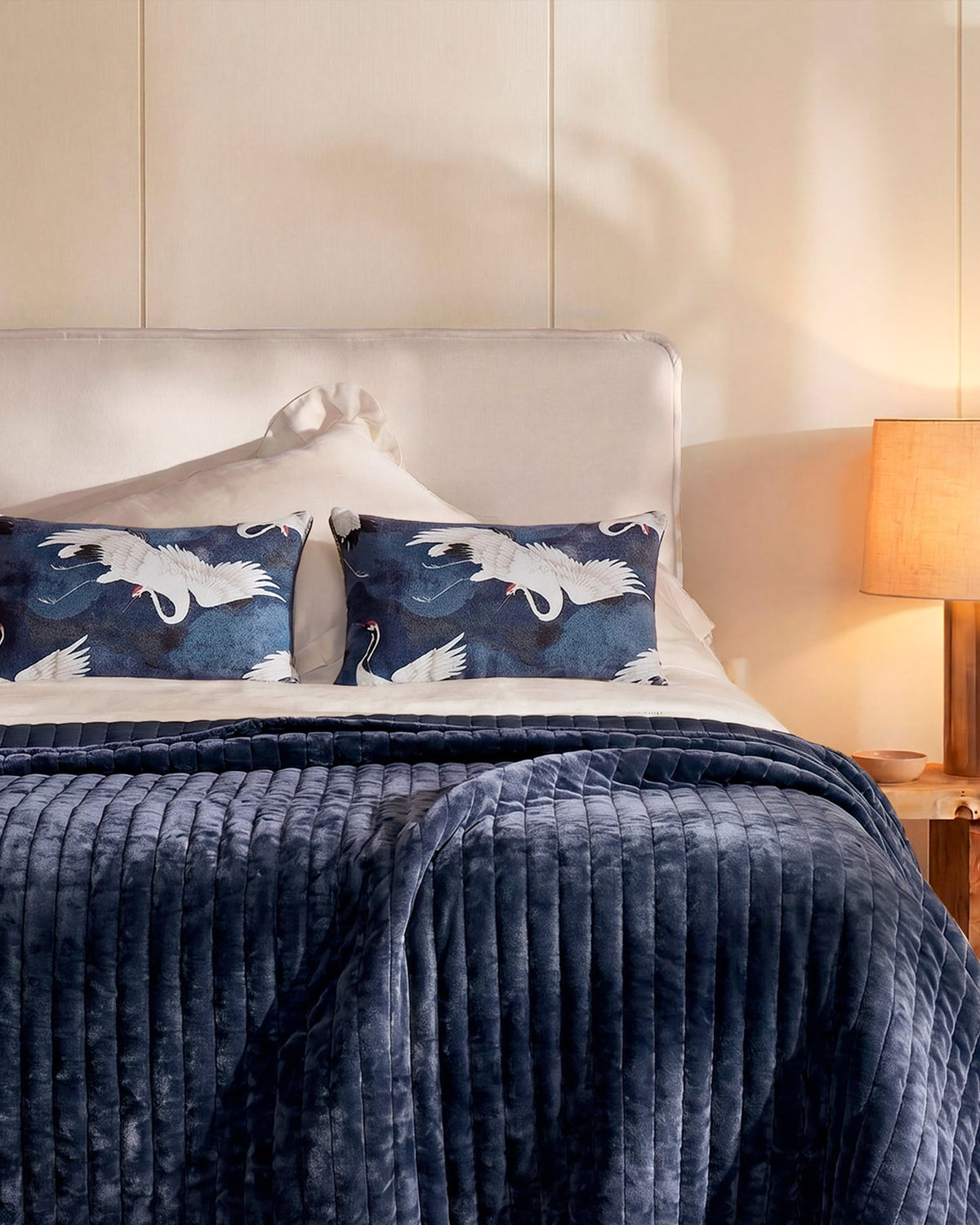 Set of dark blue lumbar pillows with white crane print on a bed.