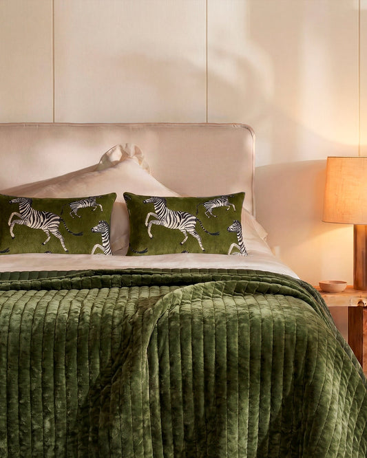 Olive green velvet quilt draped on a bed with channel stitching texture.