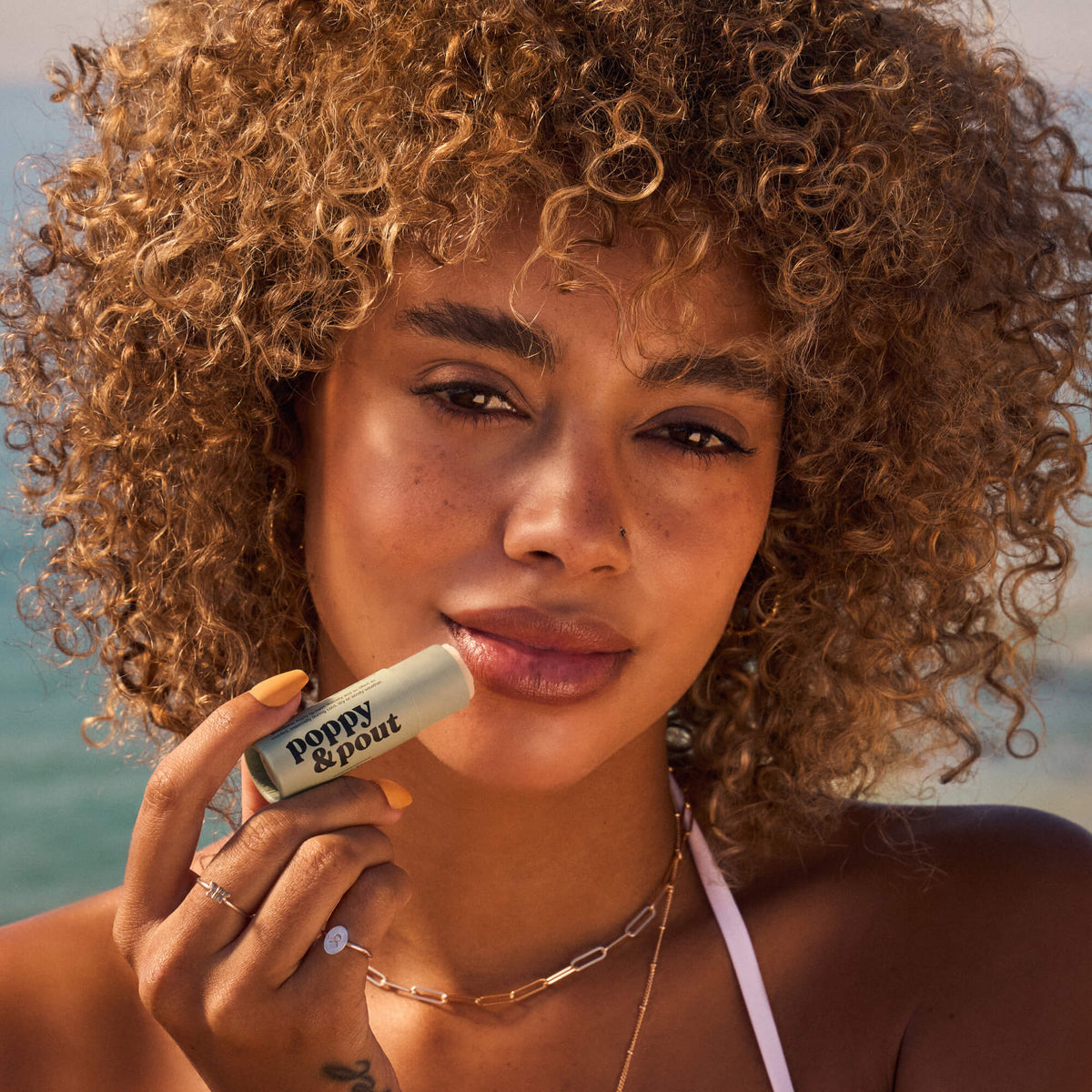 Sweet Mint lip balm tube held near lips on a model with curly hair