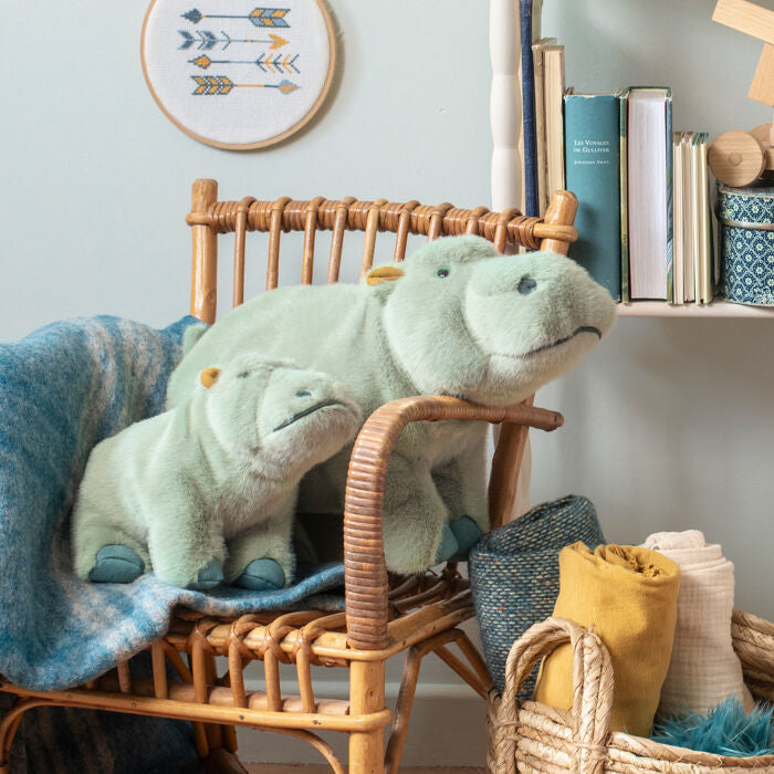 Two light gray hippopotamus plush toys on a wooden chair, blue feet and tags visible.