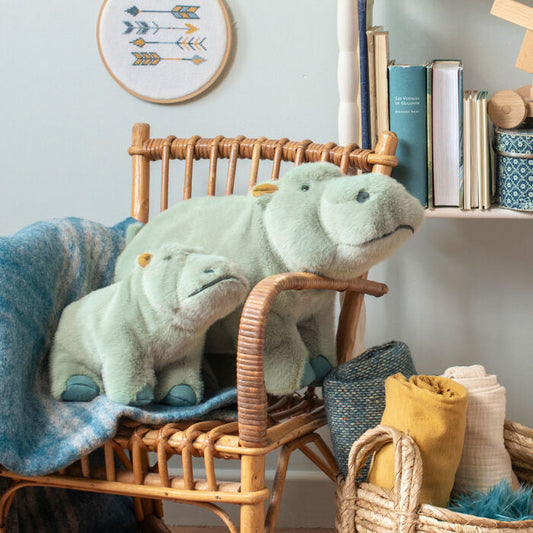 Two light gray hippopotamus plush toys on a wooden chair, blue feet and tags visible.