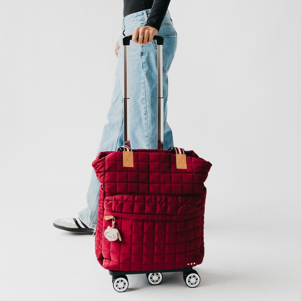 Quilted roller tote bag in red with tan handle patches, rolling wheels, zipper pocket