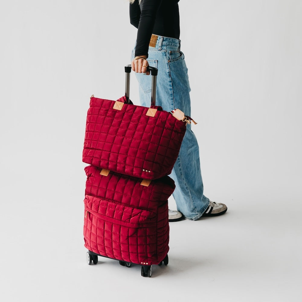 Quilted roller tote bag in red with tan handle patches and rolling wheels
