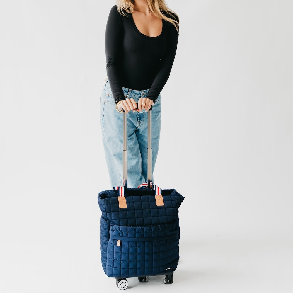Quilted roller tote bag in dark blue with tan handle patches and rolling wheels