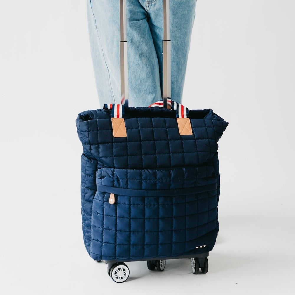 Quilted roller tote bag in navy with tan handle patches and four rolling wheels