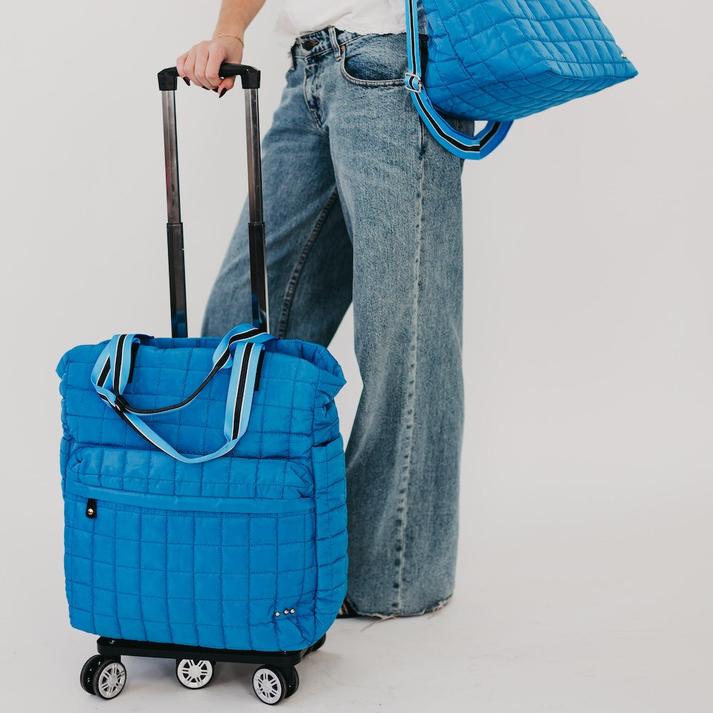 Quilted roller tote bag in bright blue with long strap, rolling wheels, side pocket