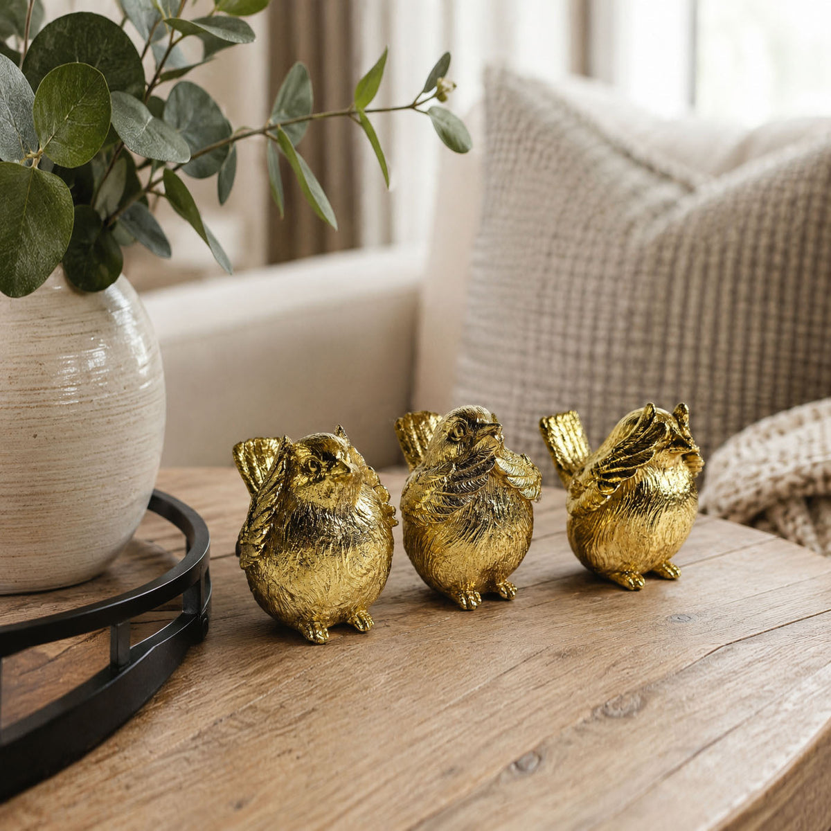 Gold-tone three bird figurines in a row on a wooden tabletop