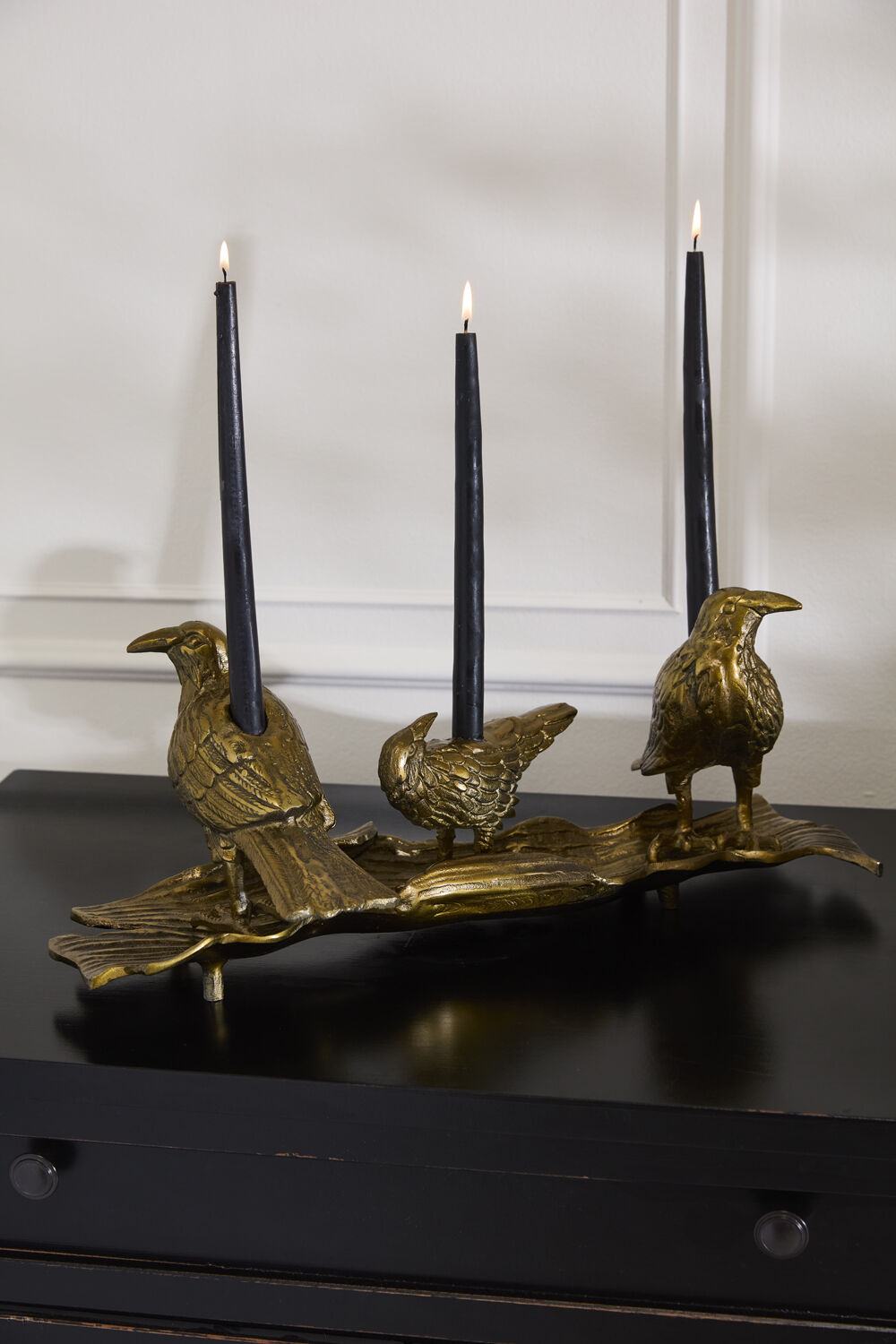 Gold-toned bird candleholder with three upright black candles on perch base