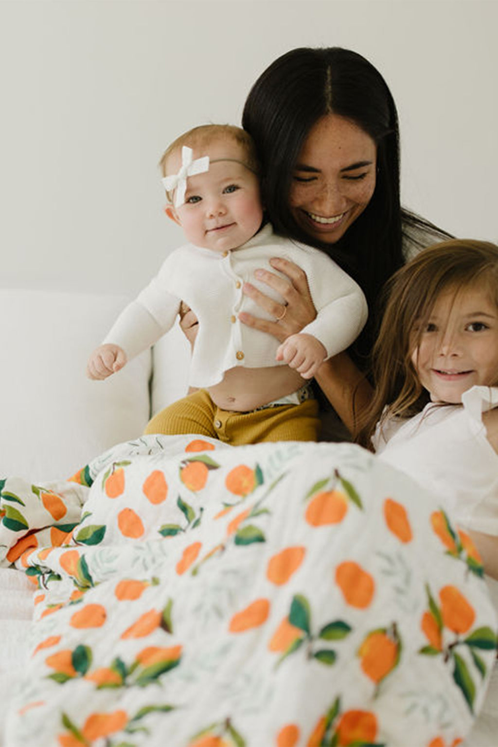 White throw blanket with orange clementine and green leaf print, draped over family
