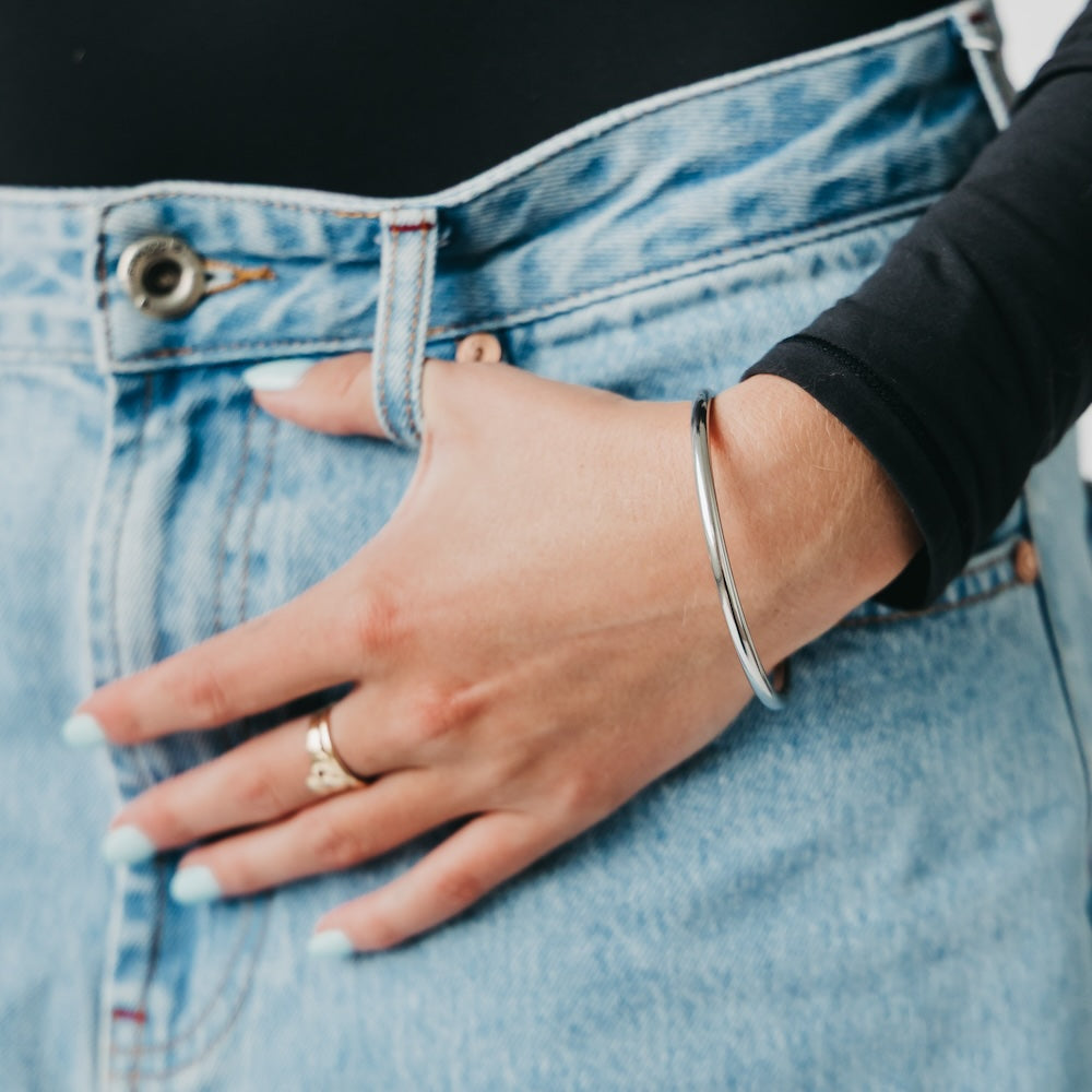 Silver bangle bracelet worn on wrist, smooth round cuff