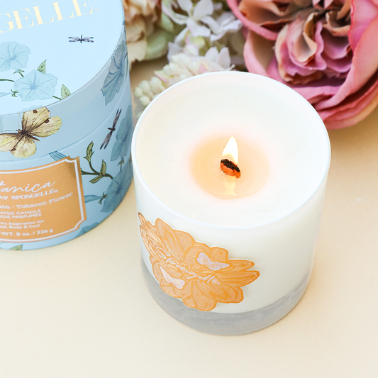 Botanica candle in white glass jar with floral design and lit wick