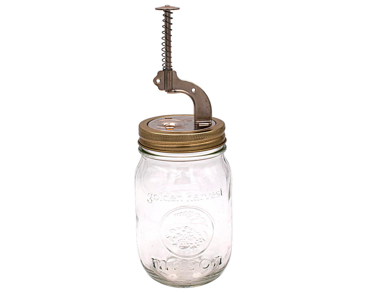 Bronze-tone cherry pitter with vertical spring handle on clear mason jar