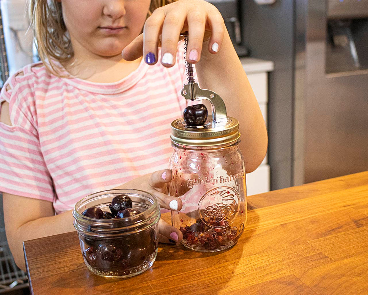 Cherry pitter pressing lever over mason jar filled with cherries