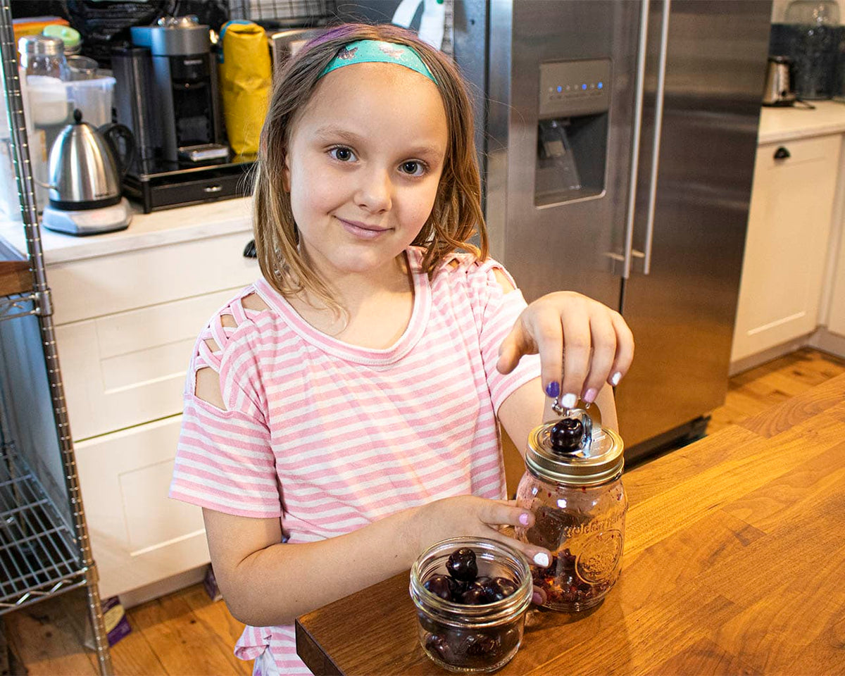 Cherry pitter in use with push-button lever over mason jar on wooden table