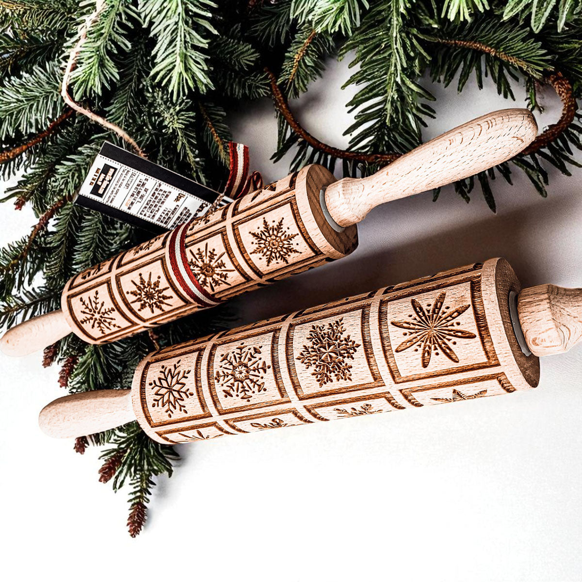 Two wooden Christmas rolling pins with light geometric snowflake pattern, hanging on a tree.