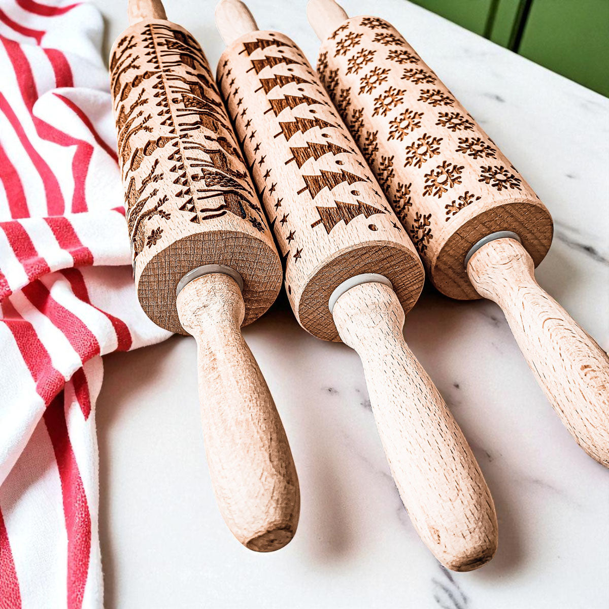 Set of three wooden Christmas rolling pins with dark festive patterns on cylindrical barrels.
