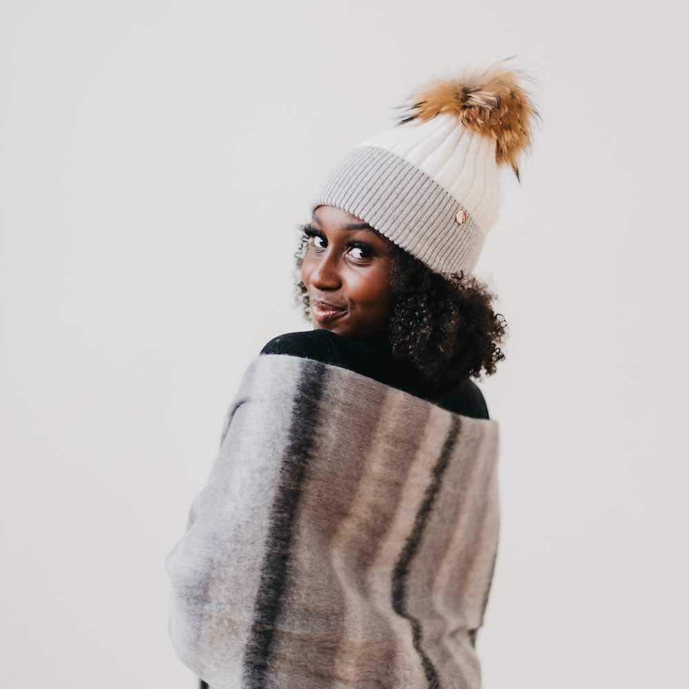 Two-tone knit beanie with tan fur pom; light knit cap and darker trim