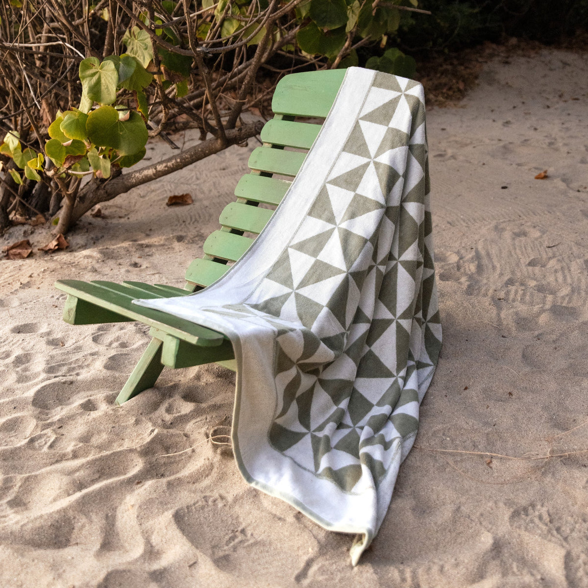 Sage and ecru geometric cotton towel draped over a green lounge chair outdoors.