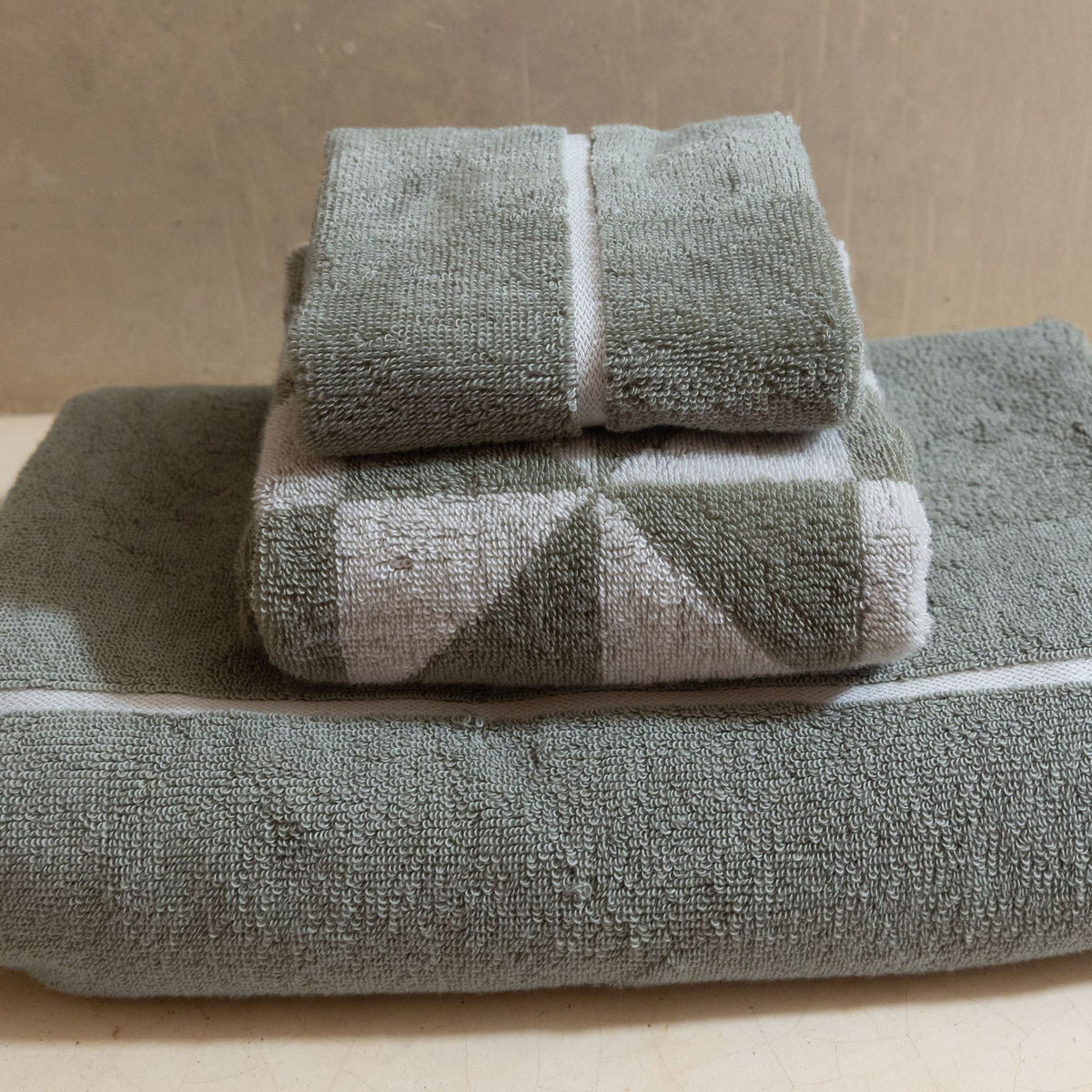 Sage-green cotton towels with white stripe edging, stacked set on surface