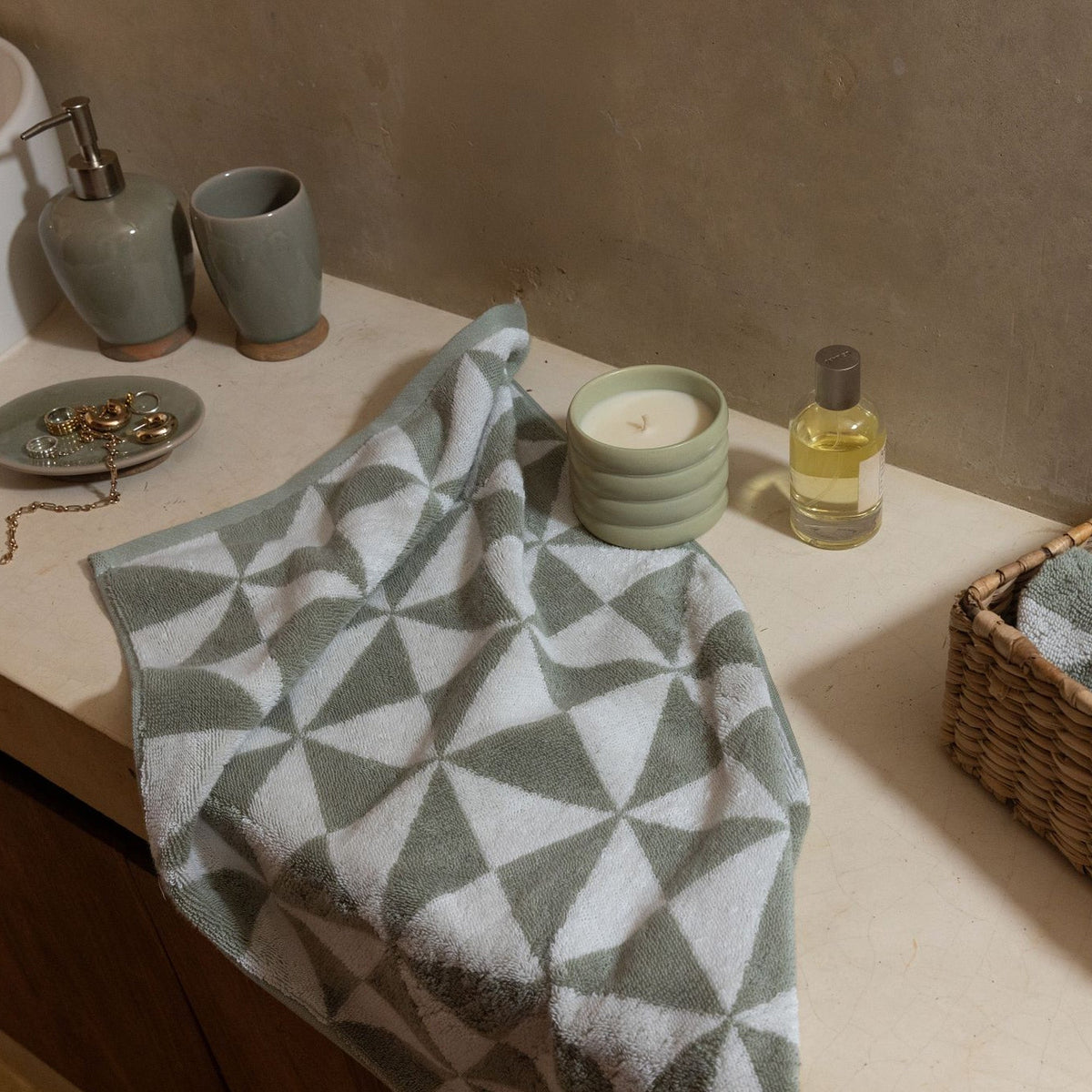 Geometric cotton towel with sage green and ecru triangle pattern on a countertop.
