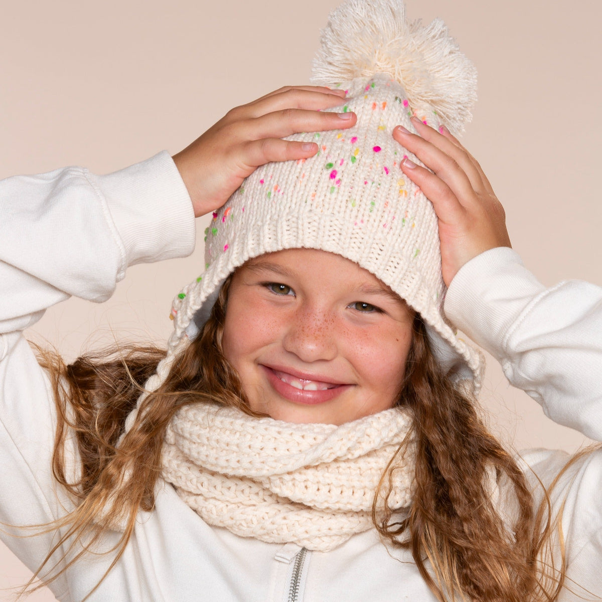 Girls' cream flecked knit earflap hat with pom-pom, worn on a child