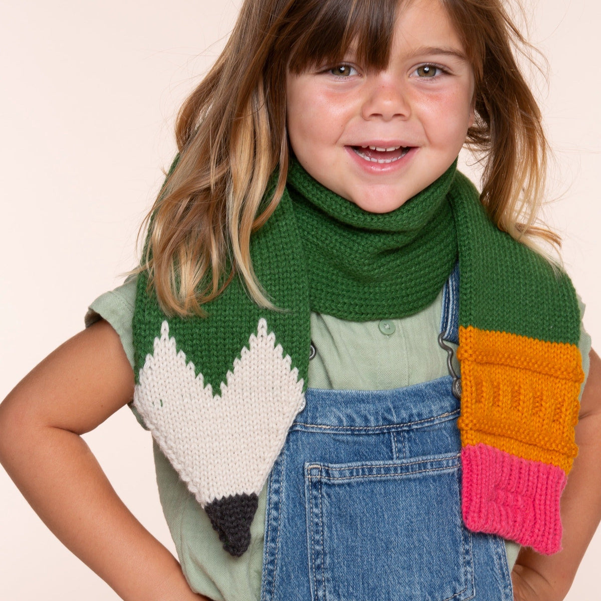 Green knitted pencil-shaped scarf worn by a child, with cream point and colorful ends