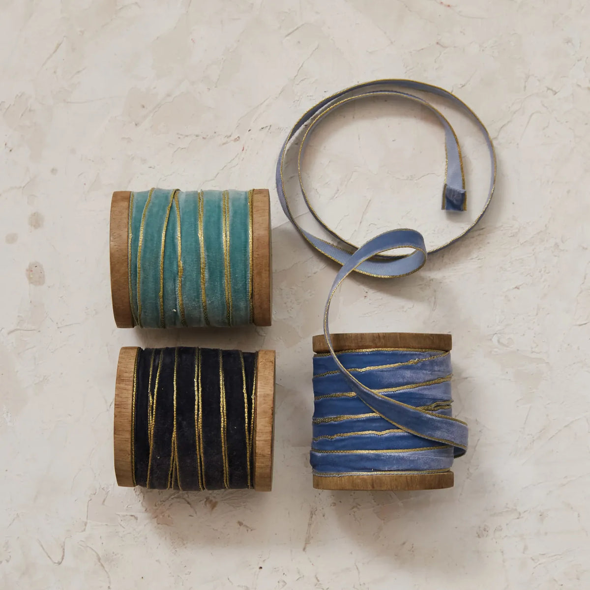 Velvet ribbon with metallic edge spools in blue tones, shown on wood rolls