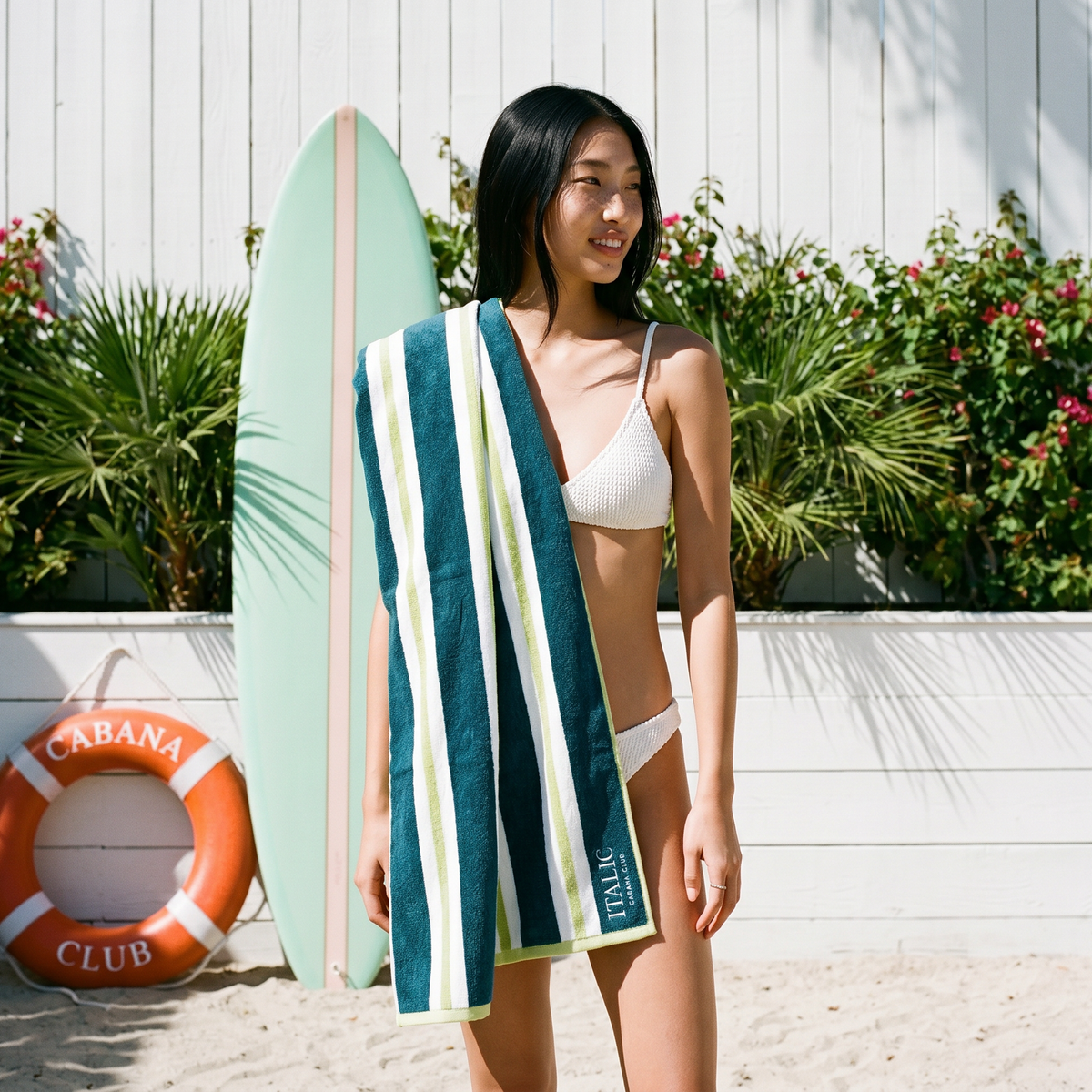 Cotton beach towel with teal and white stripe bands, folded over a standing model
