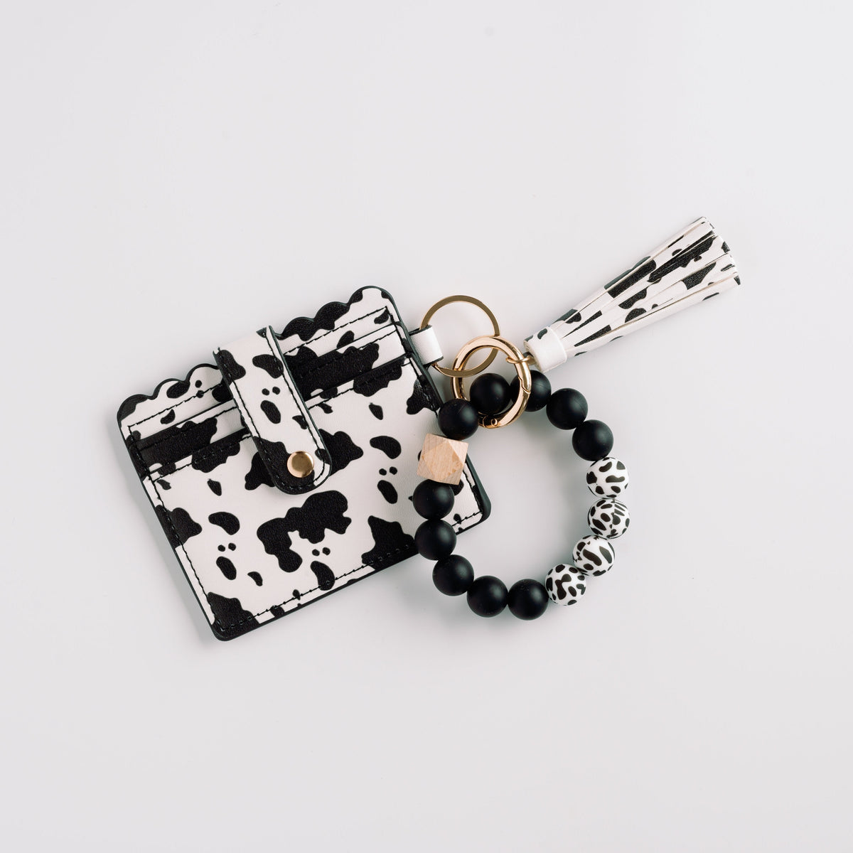 Cow print wallet wristlet keychain with black beaded bracelet and striped tassel.