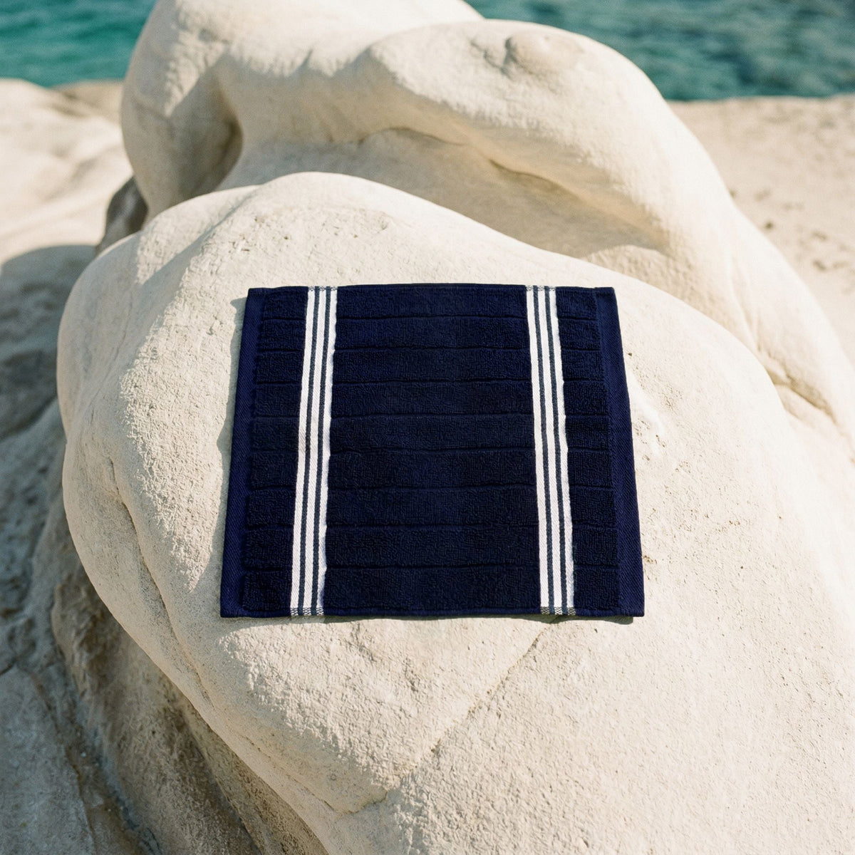 Navy cotton towel with white vertical stripe border, folded square on a light fabric
