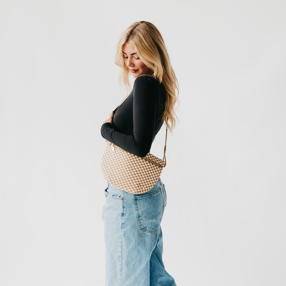 Woven checkered bum bag in tan and white, worn at the hip with crossbody strap.