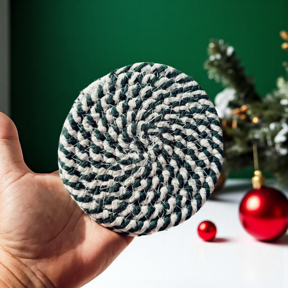 Single round dark green-and-cream striped braided rope coaster held in hand