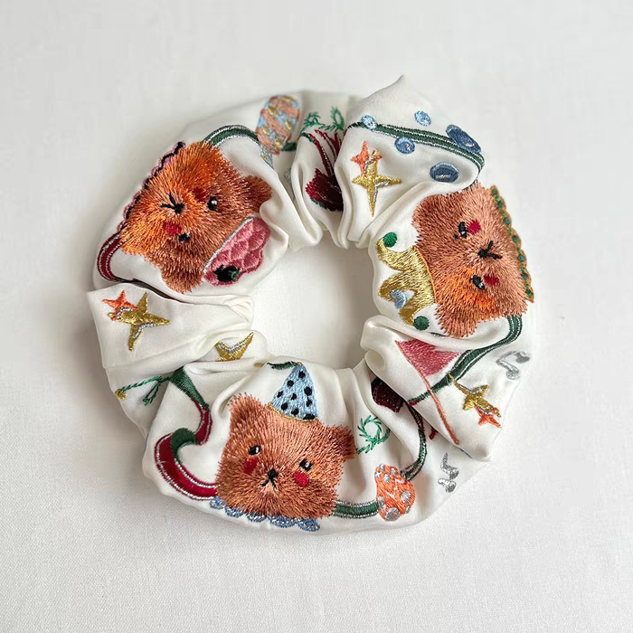 White scrunchie with embroidered circus bear faces, stars, and small circus icons
