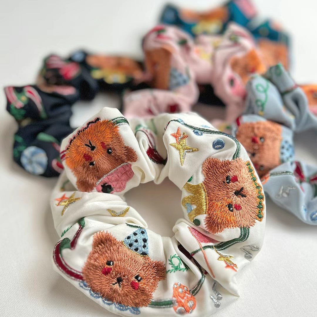 Cream scrunchie with embroidered circus bear faces, stars, and small circus icons