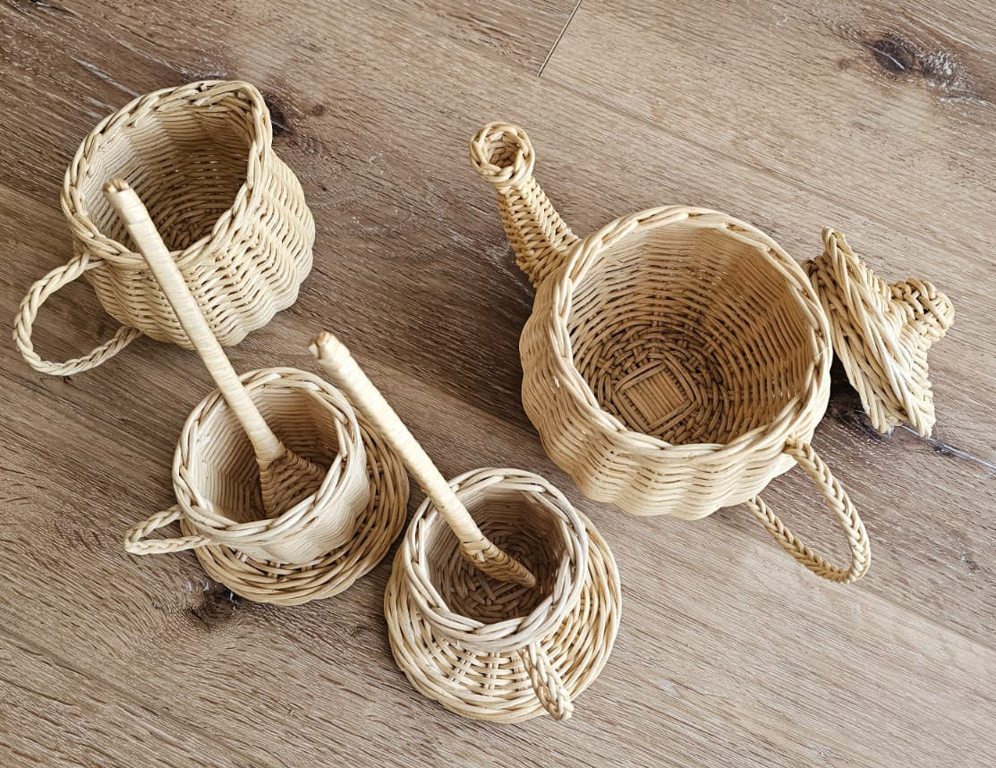 Wicker tea set with open teapot, lid, three cups, saucers and stirrers