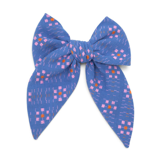 Blue fabric hair bow with multicolor square pattern, tied in a wide looped knot.