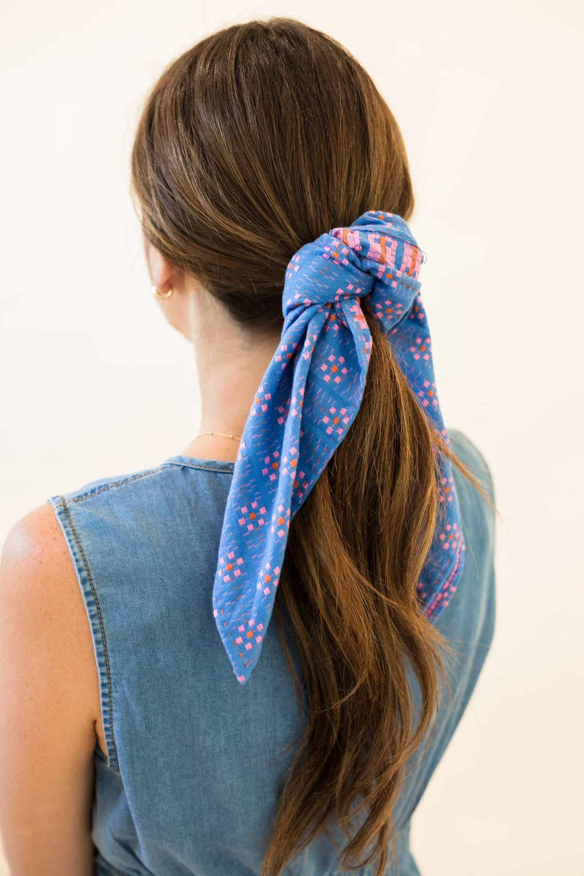 Women's blue bandana tied in hair, with pink and orange diamond pattern