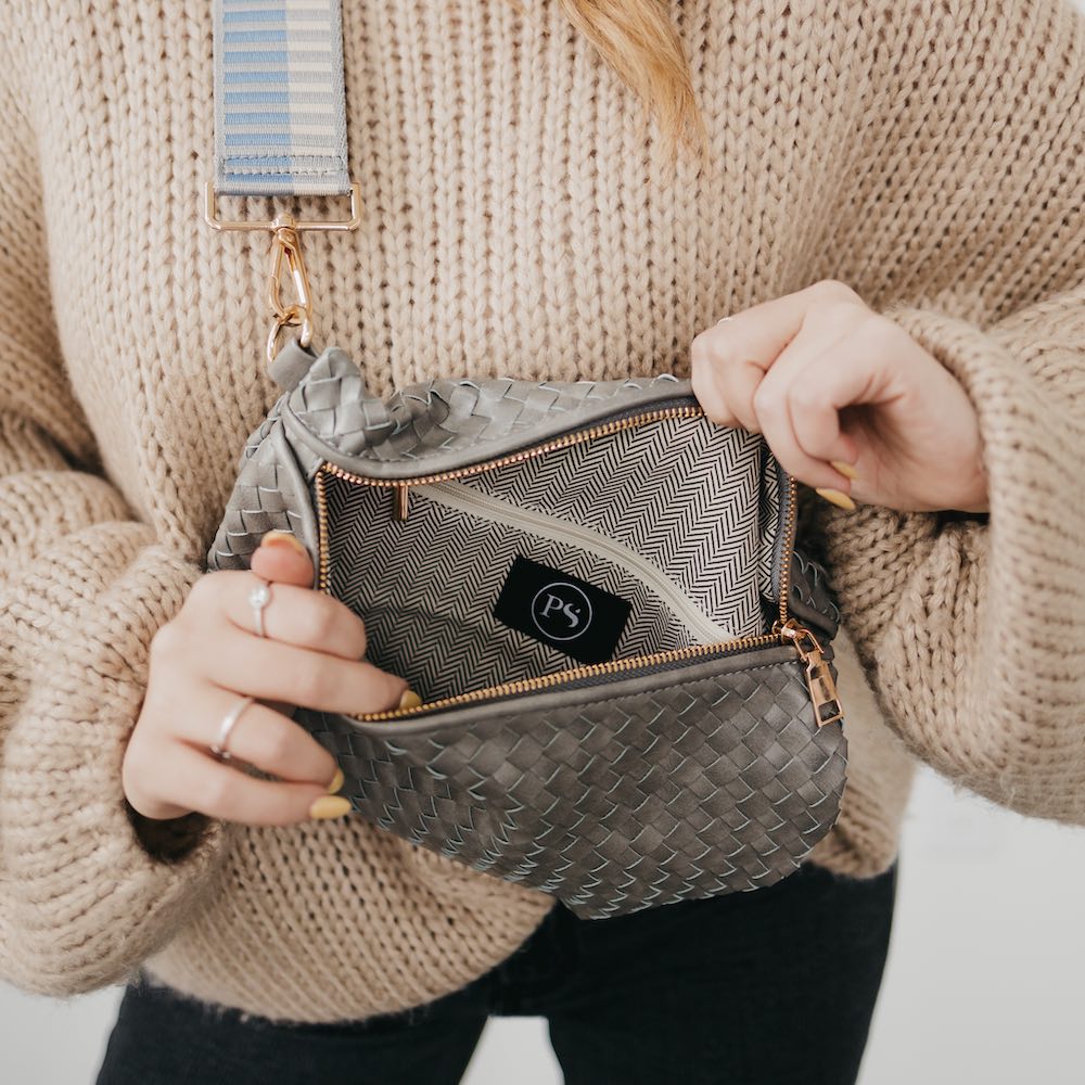 Gray woven bum bag close-up with small black logo patch and gold zipper pull.