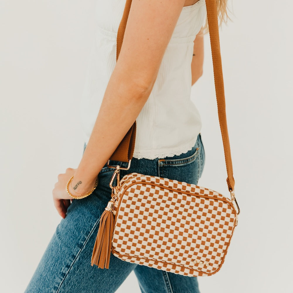 Woven checkered camera crossbody bag in tan and brown with tassel fringe and metal clasp.