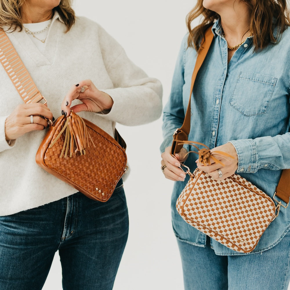 Woven camera crossbody bag in rust brown with tassel keychain and gold hardware.