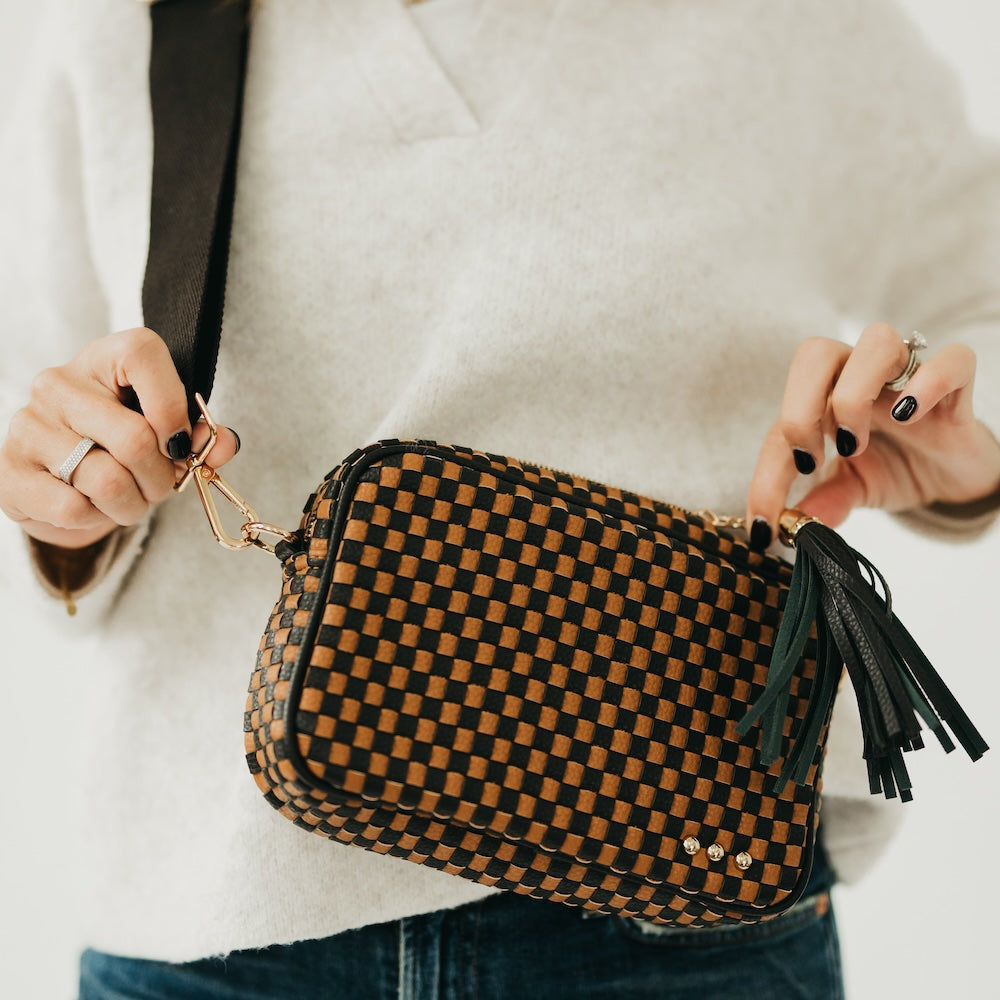 Woven camera crossbody bag with black-and-tan checkered pattern and tassel fringe